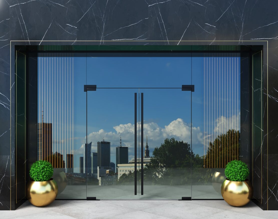 Na tym obrazku możemy podziwiać nowoczesne szklane drzwi w wieżowcu, które dodają mu wyjątkowego charakteru i stylu. Przejrzyste panele szkła wpuszczają mnóstwo naturalnego światła, tworząc jasne i przestronne wnętrze. Te eleganckie drzwi stanowią nie tylko funkcjonalne rozwiązanie, ale również estetyczny element, który wzbogaca całą architekturę wieżowca