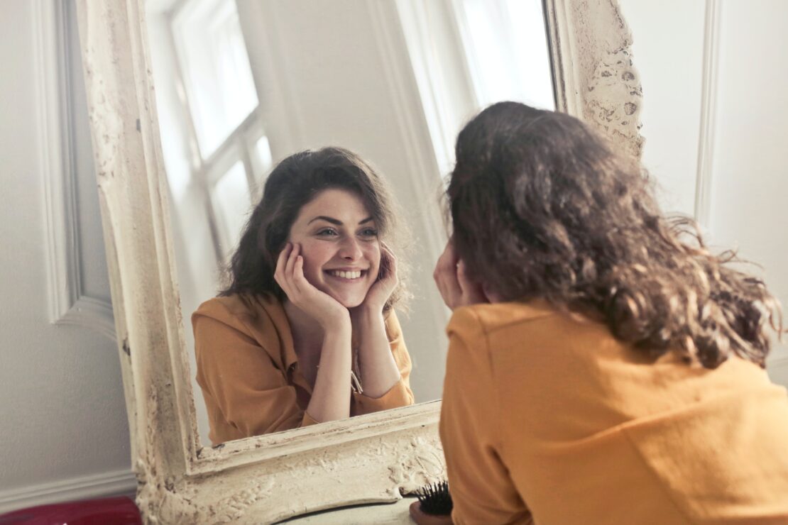 Młoda kobieta przyglądająca się i uśmiechająca do lustra w stylu prowansalskim